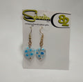Earrings with a big clear heart that is filled with blue and white flowers.