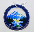 Dark blue circular ornament with the beautiful mountains and a columbine flower front and center. 