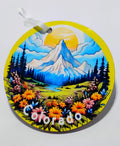 a yellow circular ornament with a beautiful mountain scenery, big sun and a field of flowers