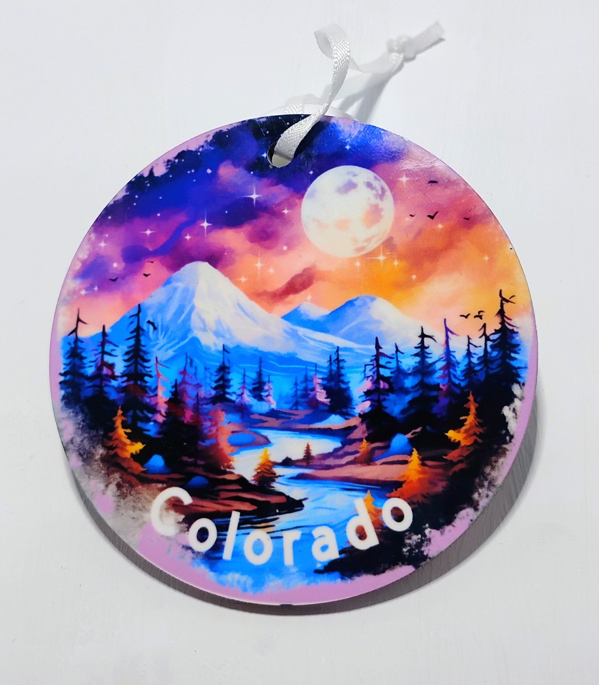 A circular ornament with a beautifully colored night sky and mountains with a river in the foreground.