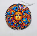 A circular ornament with a beautiful sun on the front, surrounded by so many colors. 