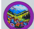Purple circular magnet with an image of a beautiful valley full of flowers and mountains in the background