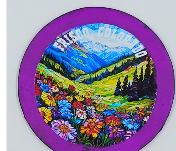 Purple circular magnet with an image of a beautiful valley full of flowers and mountains in the background