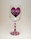 Handcrafted wine glass with a huge purple heart and the quote "Gigi, another word for love "and covered in purple polka dots. 