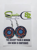 Handcrafted mandala and geometric earrings. The mandala is bright with orange and blue and a black background.