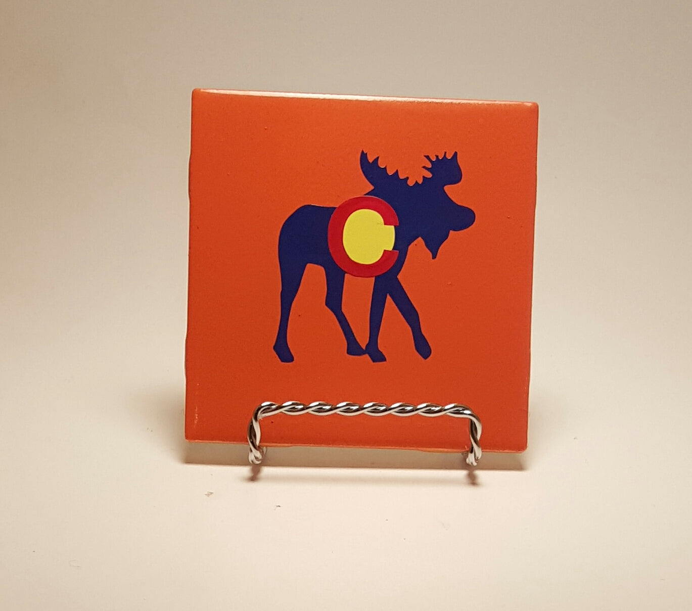 Handcrafted orange coaster with a moose design which is meant to resemble the Colorado flag.