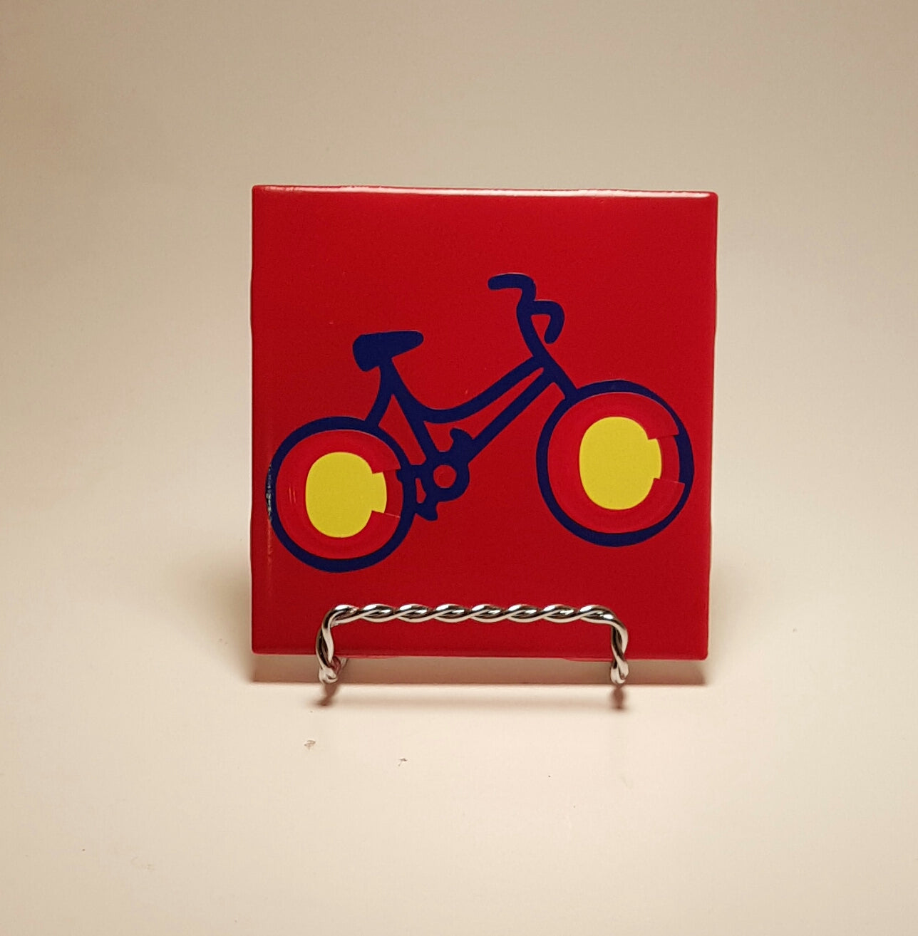 Colorful and handcrafted red coaster with a bike design, which is made to resemble the Colorado flag. 
