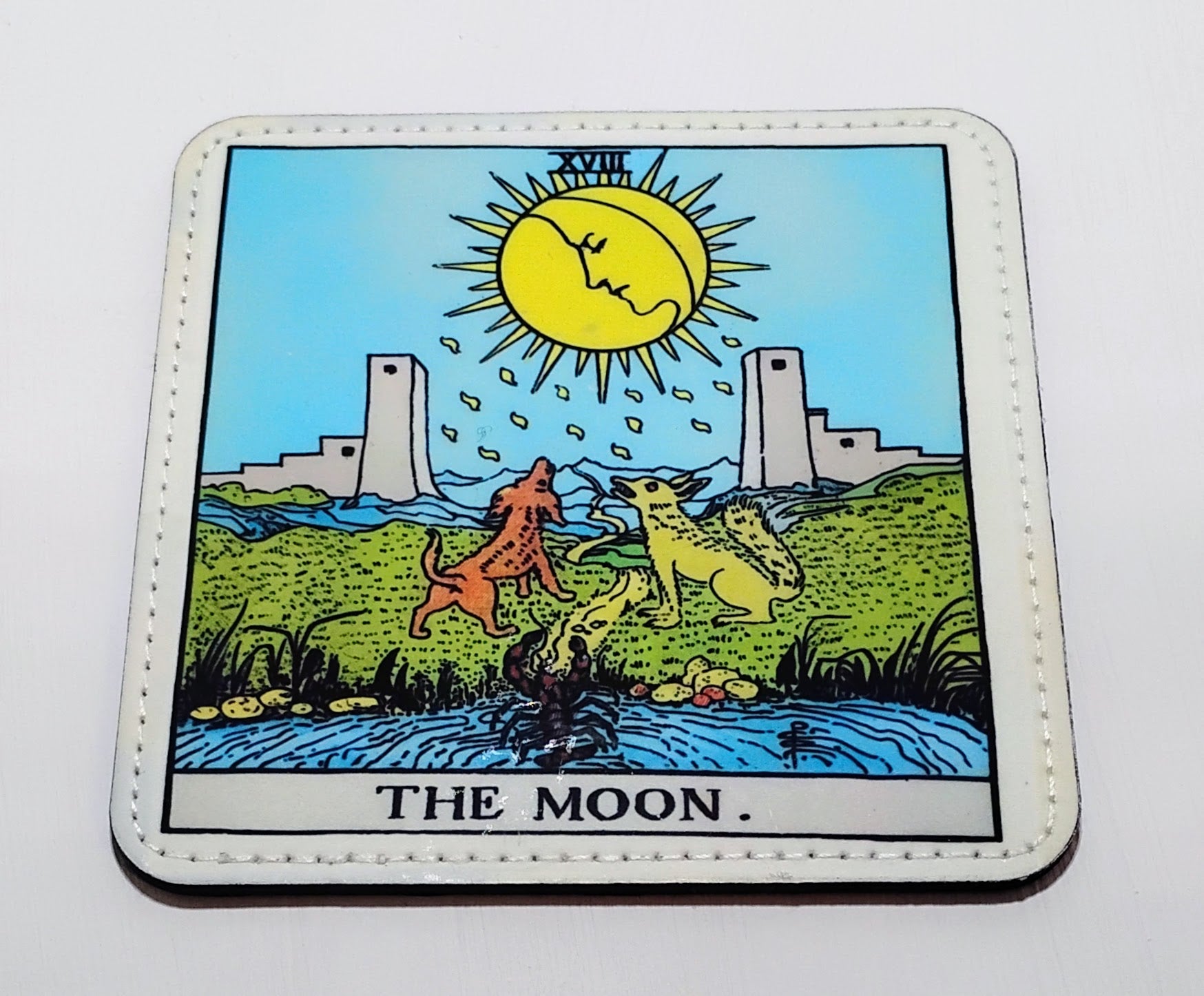 Handcrafted Coaster with 'The Moon' tarot card design featuring a sun, dogs, and buildings.