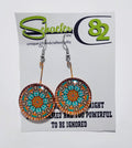 A pair of handcrafted earrings that have a mandala made out of the colors teal and orange. 