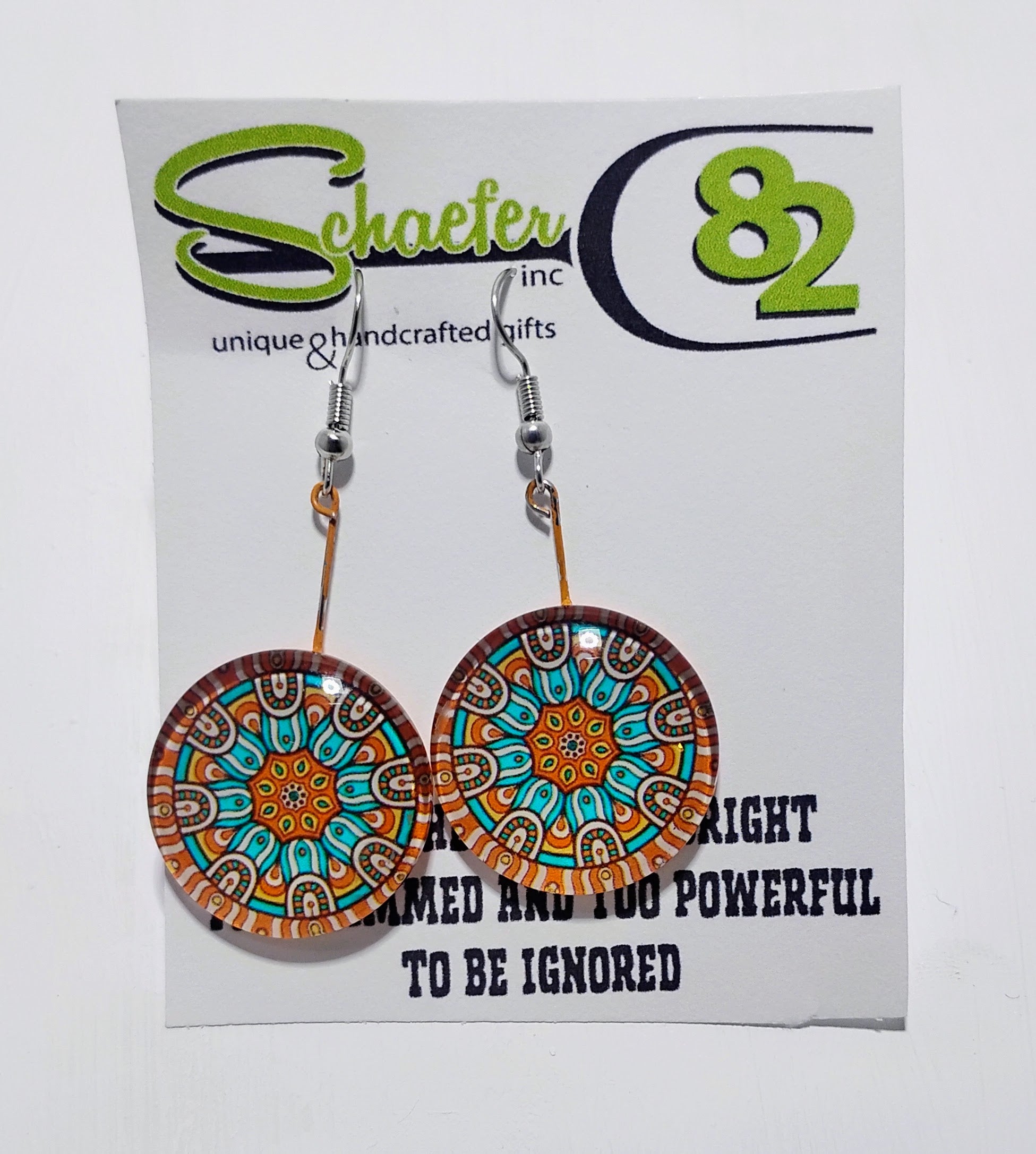 A pair of handcrafted earrings that have a mandala made out of the colors teal and orange. 