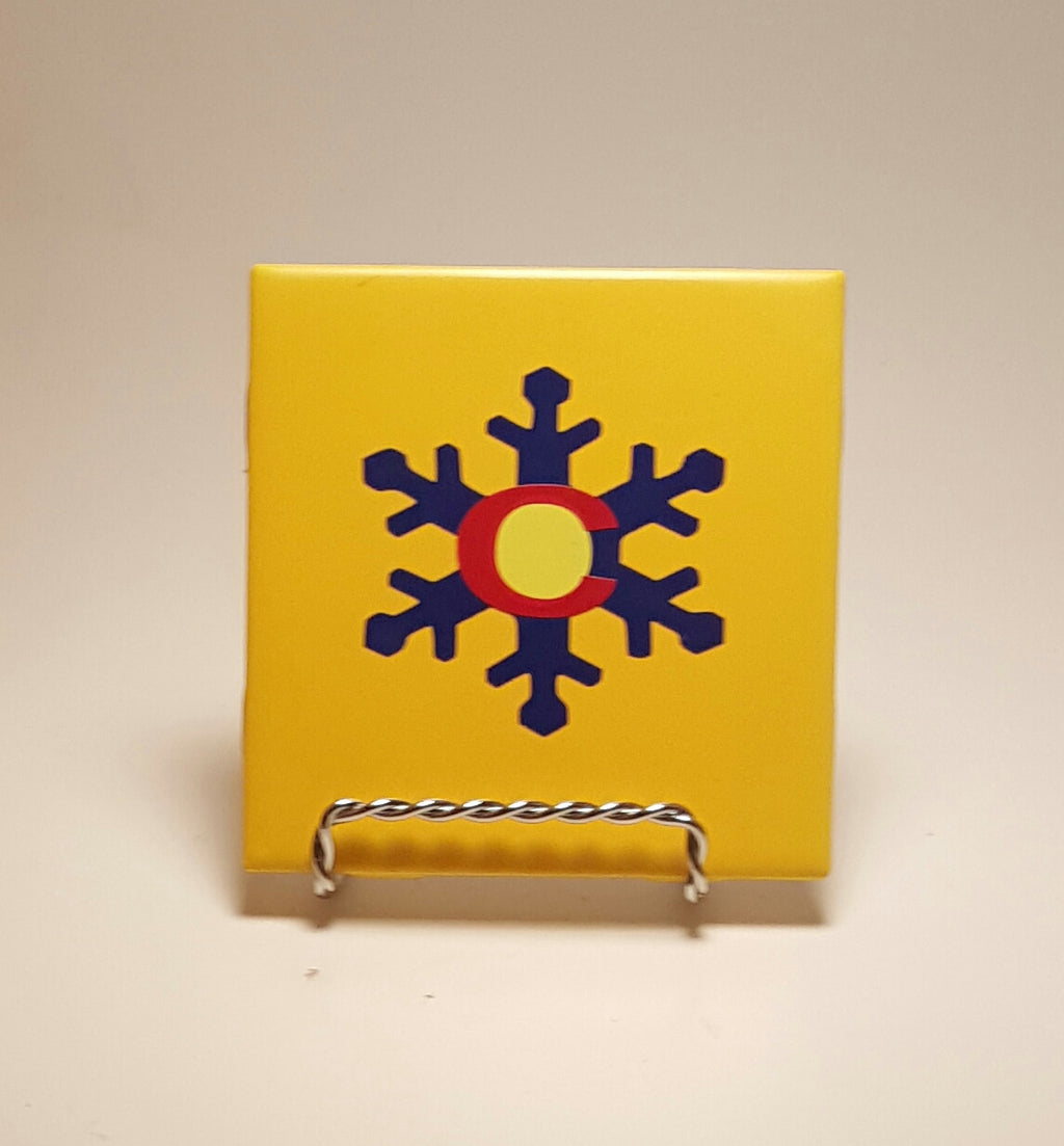 Handcrafted yellow coaster that has a snowflake design made out of the Colorado flag.