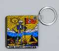 Handcrafted square keychain with a bright yellow sun and sky and a skeleton at a campsite and it says the happy camper