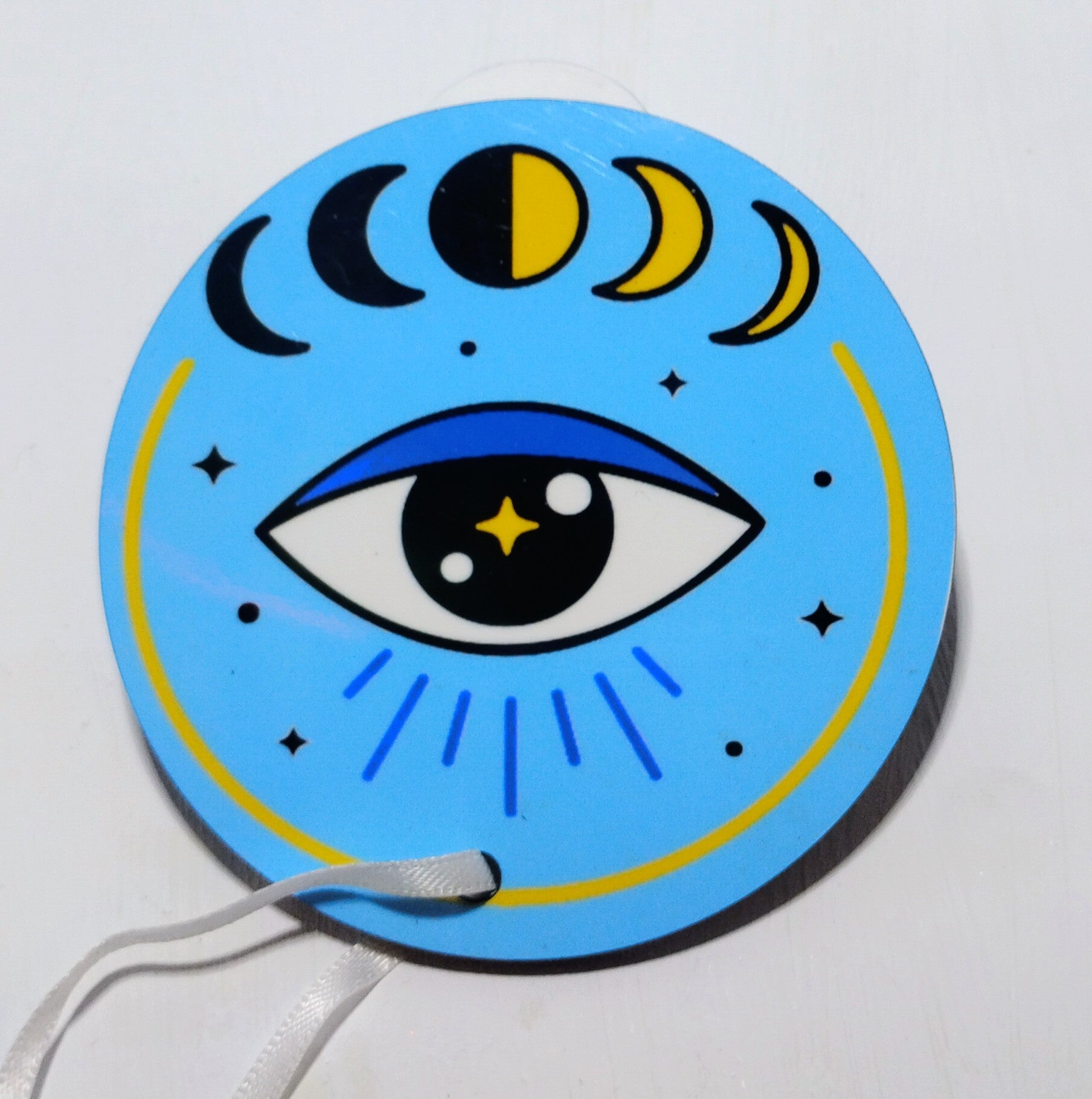 Light blue circular ornament with the image of an evil eye and the moon phases. 