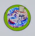 A circular lime green magnet with the image of a colorful ski slope and the saying "a little pot from Colorado" with a little pot accent
