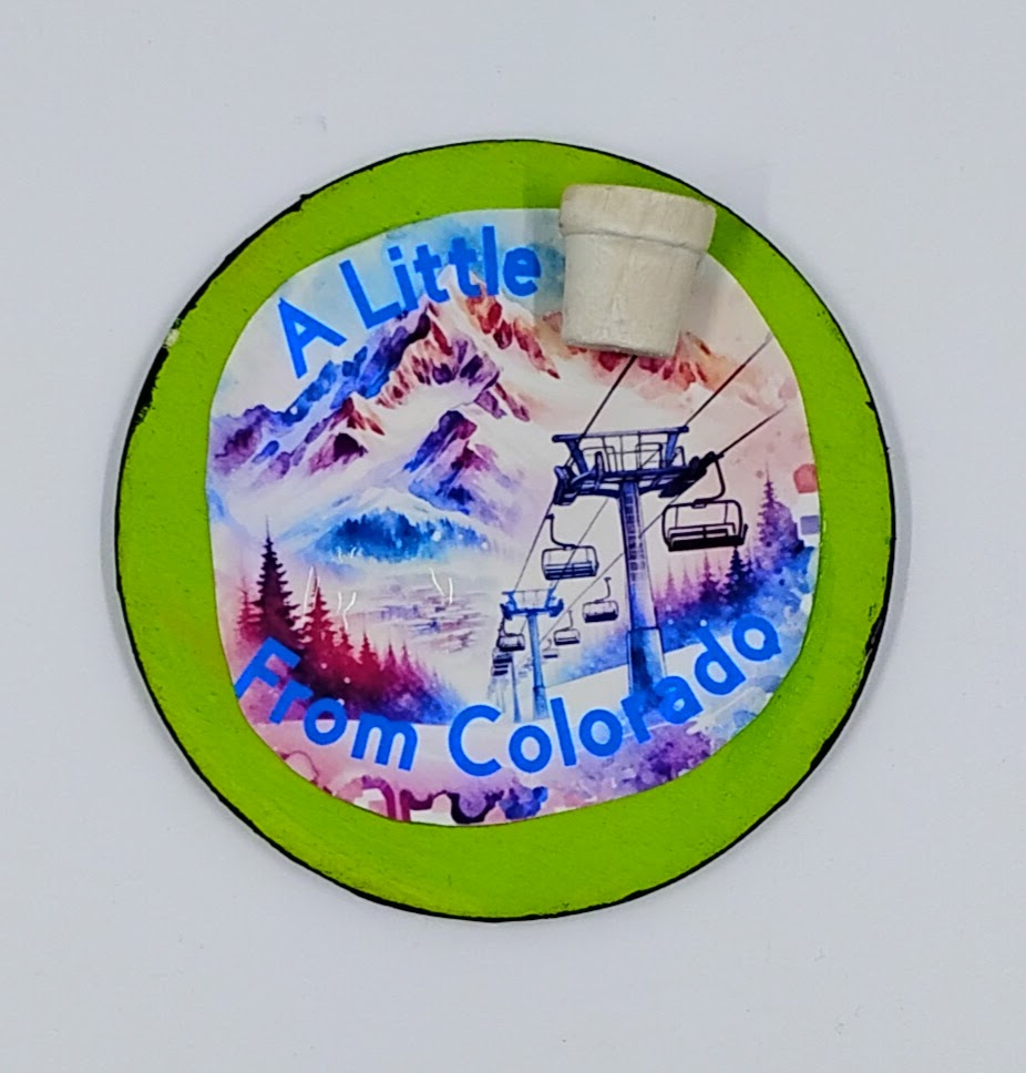 A circular lime green magnet with the image of a colorful ski slope and the saying "a little pot from Colorado" with a little pot accent