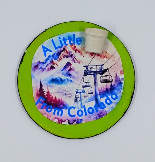 A circular lime green magnet with the image of a colorful ski slope and the saying "a little pot from Colorado" with a little pot accent