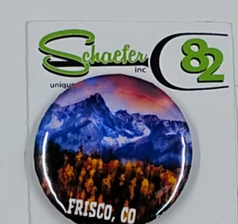Small circular hat pin with a beautiful mountain scene and yellow tress in the foreground. Plus a pink sky