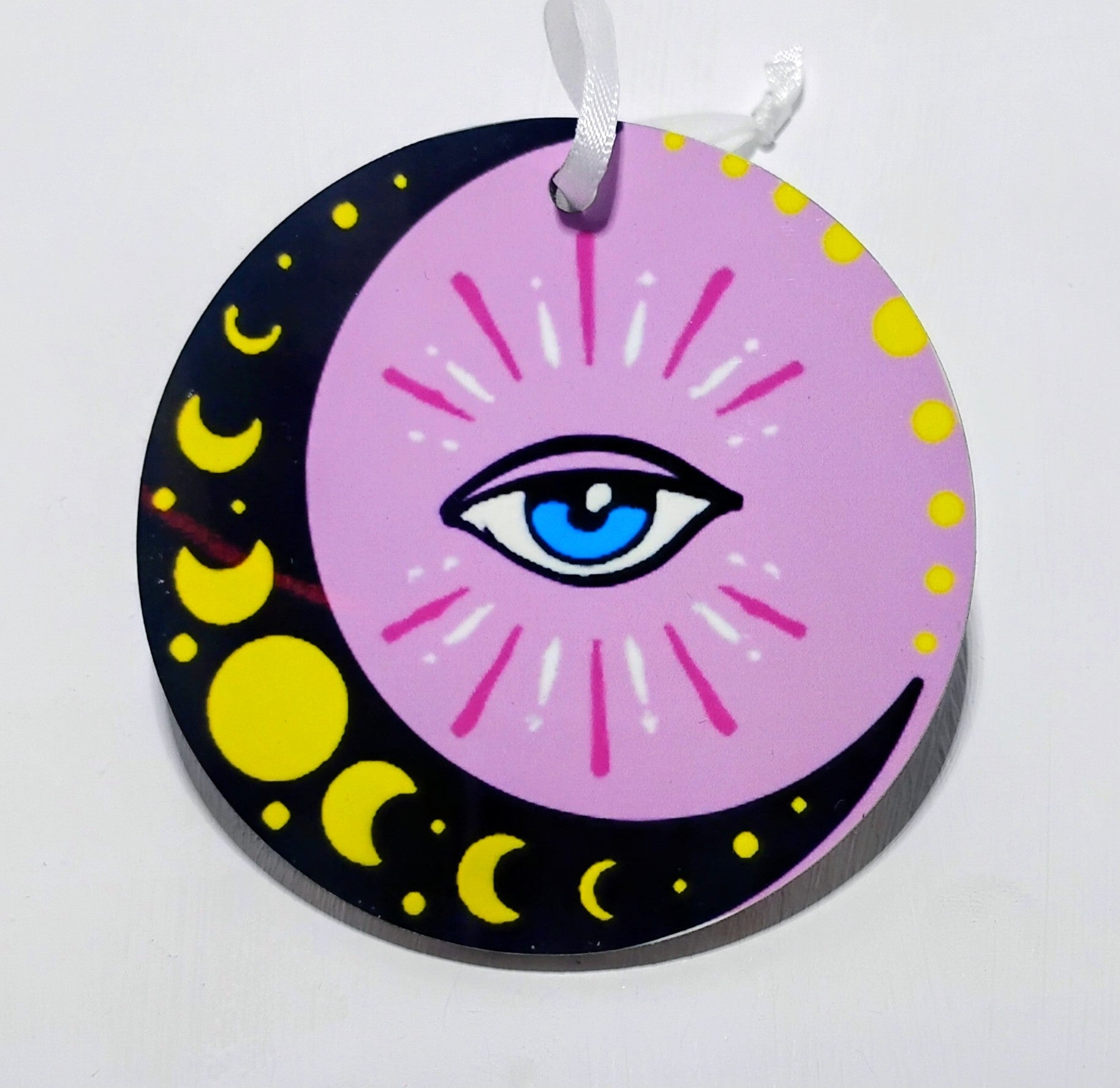 Pink circular ornament that has a black moon with all the moon phases and an evil front and center. 