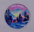 Beautiful round handcrafted coaster with a purple sky and beautiful mountains, all covered in snow.
