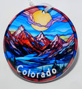 Handcrafted mountain ornament with red mountains, blue skies and a big yellow sun.