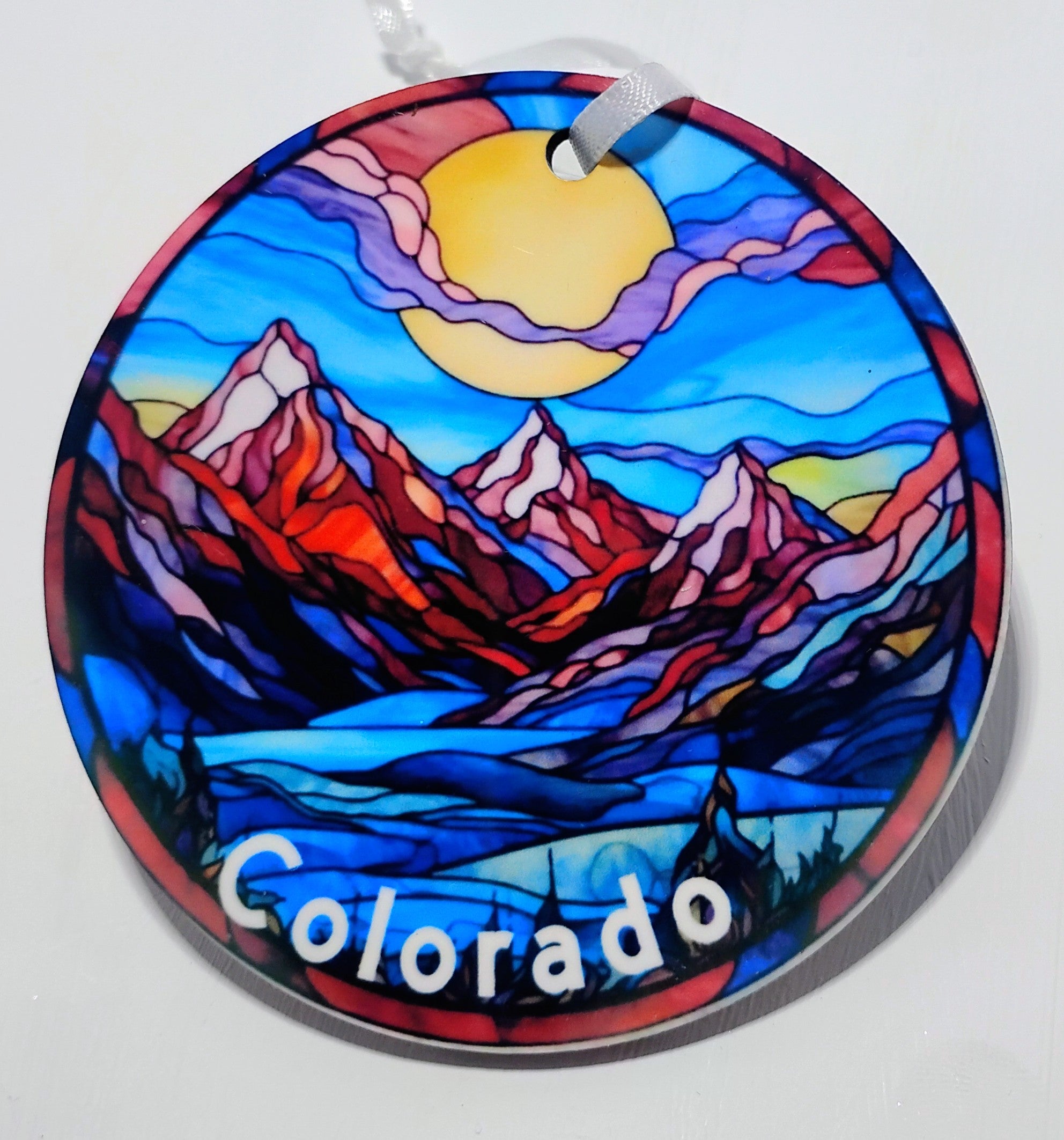Handcrafted mountain ornament with red mountains, blue skies and a big yellow sun.