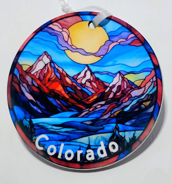 Handcrafted mountain ornament with red mountains, blue skies and a big yellow sun.