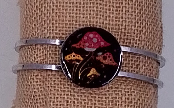 handcrafted silver bangle bracelet with the celestial design of colorful mushrooms on a black backdrop. 