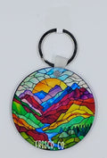 A very colorful keychain inspired by stained glass with colorful mountains and a river